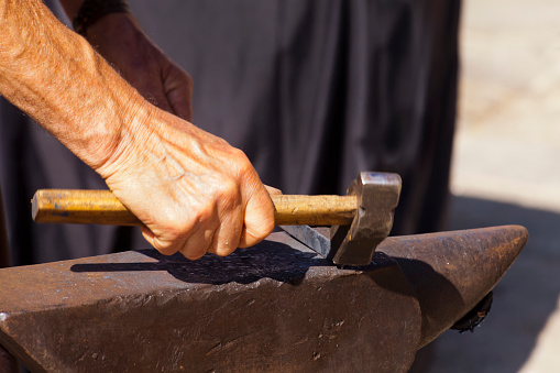 Blacksmith working, man hand holding hammer on anvil. Medieval Historical Reenactment, San Froilán celebrations,  Lugo city, Galicia, Spain.