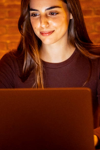 istock Beautiful Authentic Young Woman Sitting at a Table in Cozy Kitchen and Using Laptop Computer at Home at Night. Female Smiling and Chatting on the Internet and Social Media, Doing Online Research. 2145287765