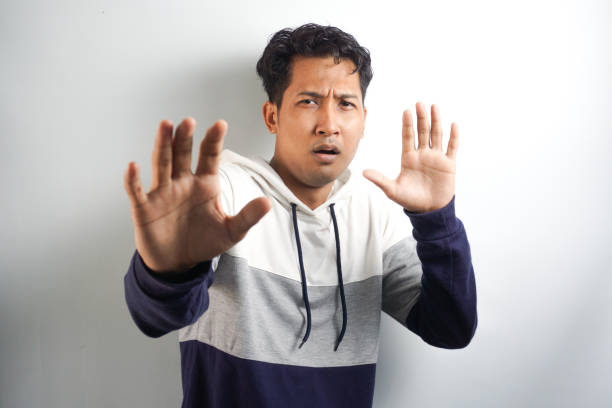 Attractive young man makes frightened gesture with palms, defends himself from someone, asks to stop it immediately. Guy says stay away from me, shows stop sign. Body language concept