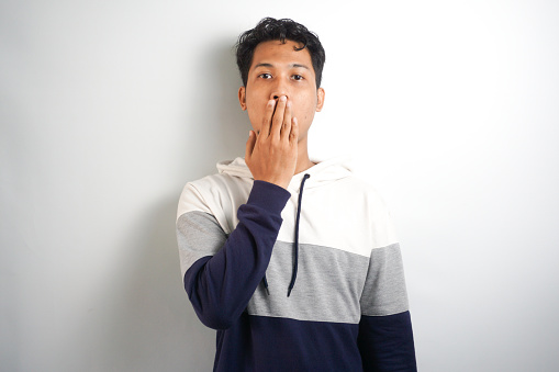 Shocked worried, embarrassed young man said something he shouldnt have, shut his mouth with hands and look guilty or anxious at camera, feel sorry for being rude, white background