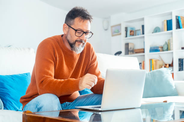 istock Handsome serious man sits on sofa with computer on laps, spend time at home web surfing information, use modern tech, make order on internet. Freelancing, telework, new software. Small online business 2145298315