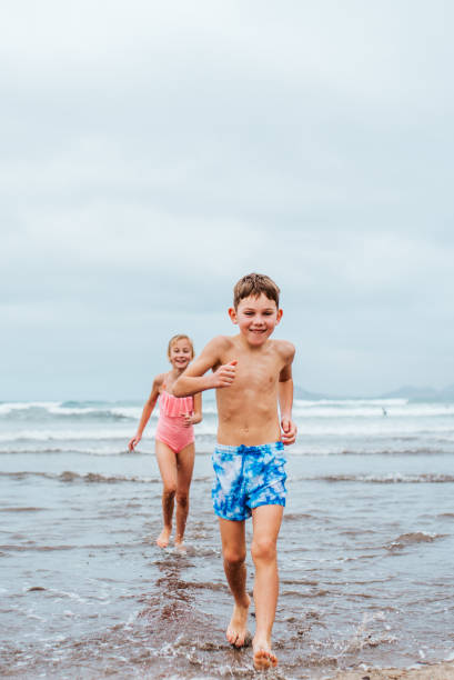 istock Siblings playing on beach, running, skipping, having fun. Smilling girl and boy ion sandy beach with vulcanic rocks of Canary islands. Concept of family beach summer vacation with kids. 2145355175