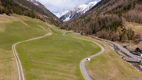 Aerial drone view of an alpine meadow during early spring time. some dirt roads are in the meadow. Steep mountain slopes and snowcapped mountains in the background. copy space available.