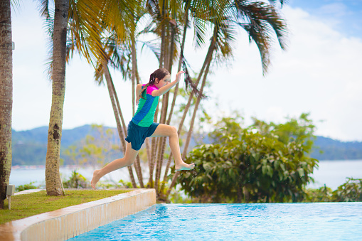 Kids jump into swimming pool. Summer water fun. Children play in outdoor pool. Summer family vacation with young kid. Holiday in tropical resort. Travel with child.