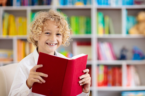 Child reading book. Kids read. Little boy at a colorful bookshelf doing homework for school. Student with books. Early education and development. Home library for children. Preschool kid study.