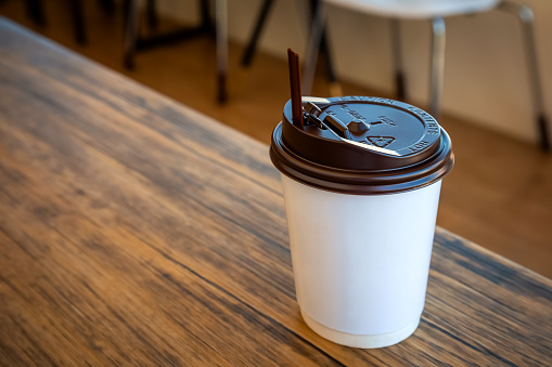 A Paper Cup of Hot Coffee with Plastic Cap Placed on the Table