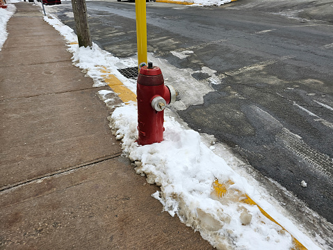 A red fire hydrant along the side of a sidewalk with some snow around it.