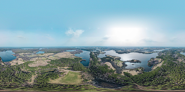 This panoramic aerial image stretches across a breathtaking landscape where a series of lakes shimmer under the sun's gentle glow. The vastness of the view is punctuated by pockets of woodland and fields, with the horizon blurring the line between earth and sky. Suitable for illustrating vast natural spaces, the harmony of ecosystems, or the quietude of rural scenery, this photograph offers a sweeping perspective on the beauty of the natural world.