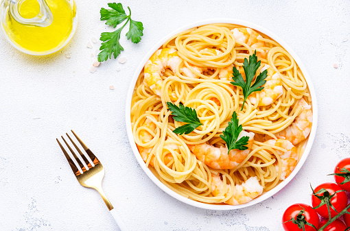 Delicious spaghetti pasta with big shrimp on plate with parsley, white table background. Top view