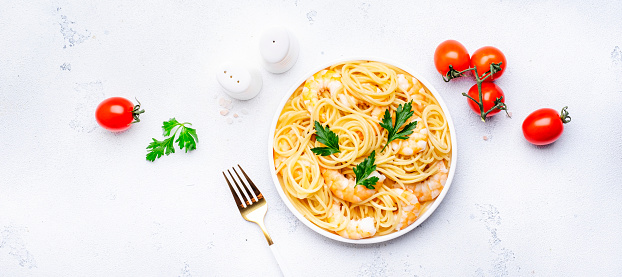 Spaghetti pasta with big shrimp, olive oil and parsley on white table background. Top view banner