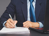 A businessman signs a document at desk in the office.