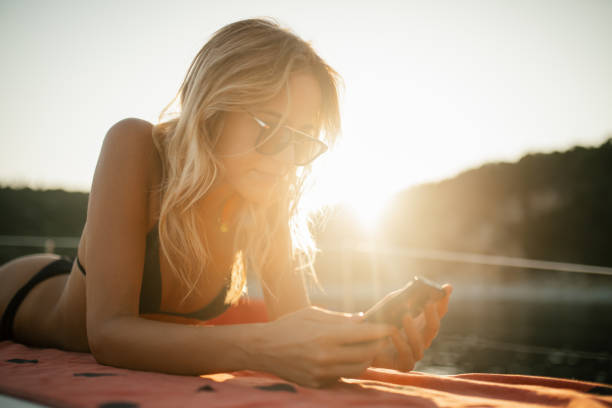 A beautiful young blond woman lying on a sailboat deck, she is smiling, looking relaxed, enjoying the moment. She is lying next to the mast