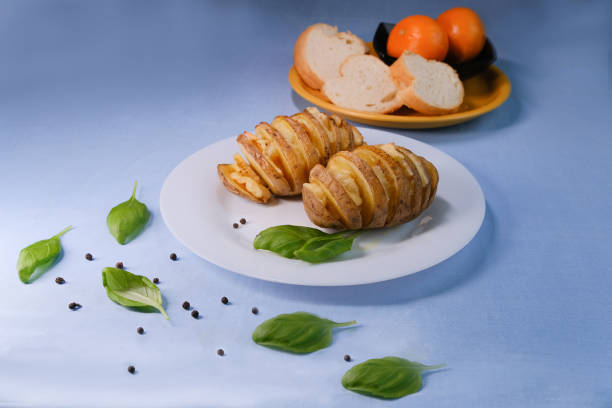 Baked potatoes with lard on a plate. With basil leaf, pepper, bread and orange