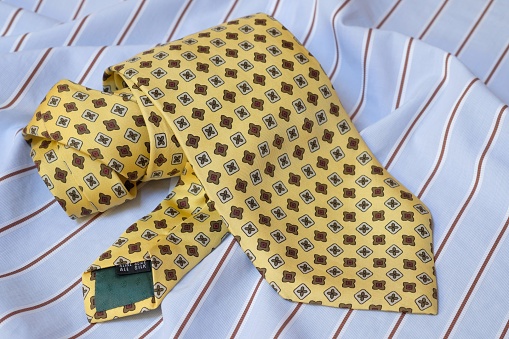 The tie is yellow and patterned, twisted. The tie lies on the surface of the blue shirt.