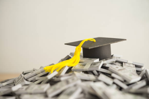 istock Graduation cap university or college degree on US dollars banknotes pile. 2145679346