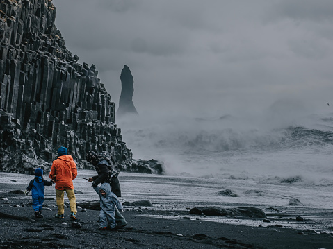 REYNISFJARA, ICELAND - MARCH 21: Tourist Family Approaching Sneaker Waves At Black Sand Beach With Strong Wind Condition At  Reynisfjara, Iceland
