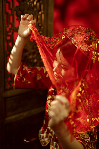 Portrait of an Asian Chinese woman in traditional bridal tea dress lifting the red veil