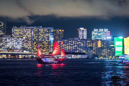 Hong Kong cityscape skyline at night with Traditional Junk Boat moving across the sea. Slow shutter speed. Pan photo