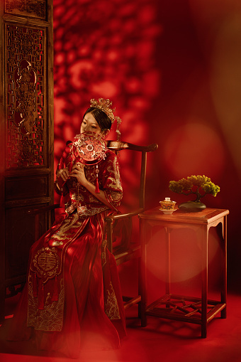 Stunning Asian Chinese woman in traditional bridal tea dress and headwear against a red background