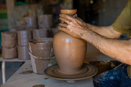 Crop male hands shaping wet clay vase on wheel while working in Moroccan pottery workshop