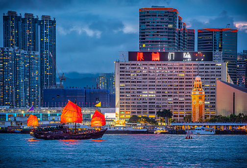 Hong Kong cityscape skyline at night with Traditional Junk Boat passing in front of Former Kowloon-Canton Railway Clock Tower