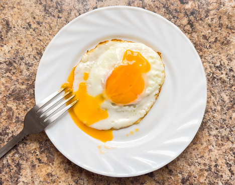 Fried egg on a white plate with a fork on the table.