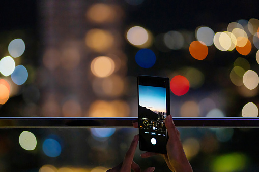 Man capturing night cityscape with mobile phone camera against a backdrop of mesmerizing bokeh lights