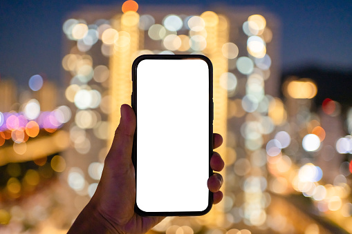 Man holding mobile phone with blank white screen against bokeh light background