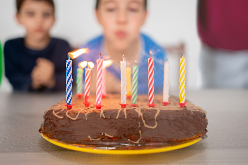 Blowing out candles on birthday cake with children in the background.Close up of candles blown on chocolate cake. Happy birthday concept. Candle smoke on homemade pie. Sweet holiday cake