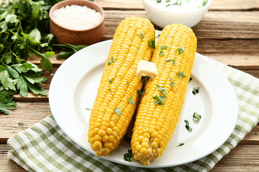 Fresh corn with parsley and butter on wooden table