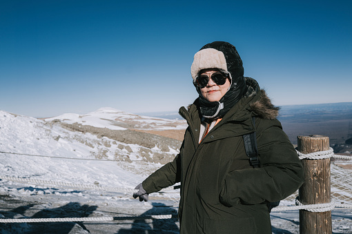 Asian Chinese mature female tourist standing in front of snowcapped mountain looking at camera  admiring scenery