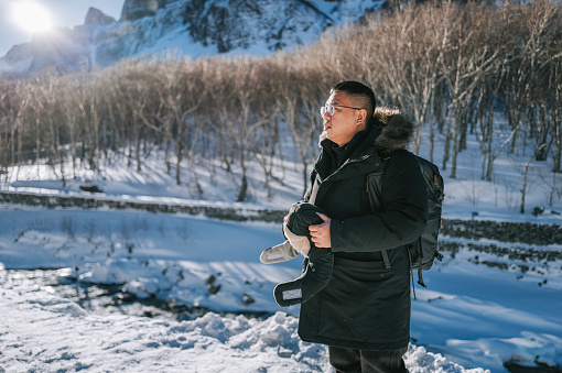 Asian Chinese mature male tourist standing in front of snowcapped mountain looking away admiring scenery
