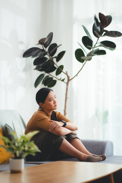 istock Asian woman feeling lonely thinking about problem sitting embracing knees on sofa. 2145834327