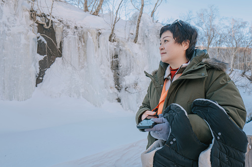 Asian female solo travel tourist standing in front of frozen waterfall , changbaisan, north china