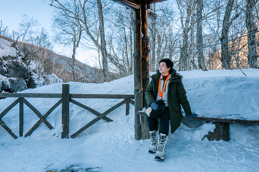 Asian female tourist in warm clothing sitting at bus stop waiting  at Chang Bai San, China in winter