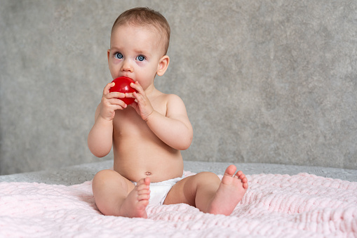 The baby is licking a small toy red ball with concentration.
