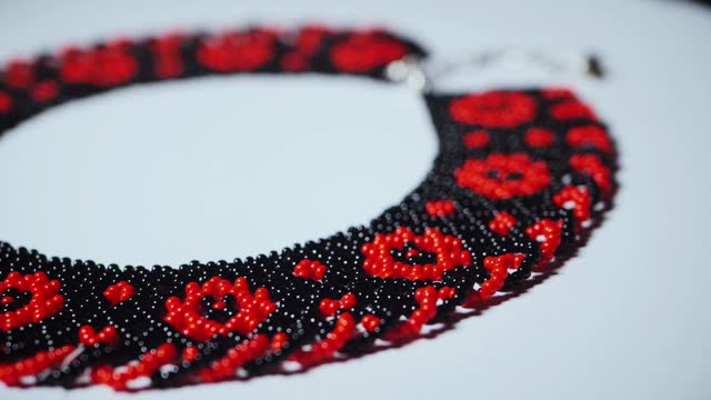 Stylish red and black necklace against white backdrop. Ukrainian Elegant accessory with red and black beads on white. Contrast of colors in beaded necklace on white. Red and black beads in necklace on clean white. Beautiful pattern and ornament