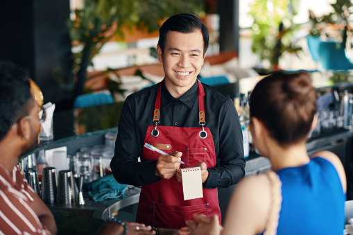 Smiling waiter talking to couple, recommending drinks and dishes of the day