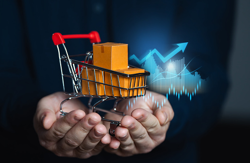 A businessman holds a shopping cart with goods against the background of growth graphs. Rising prices. Increase in supplies and production rates. Enhancement in the attractiveness of goods.