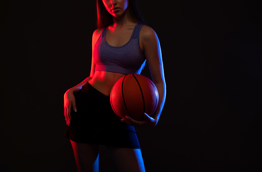 A beautiful slender girl athlete in shorts and a top plays basketball.
