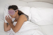 woman in her sleep mask sleeps beneath a comforting blanket, a testament to healthy sleep habits.