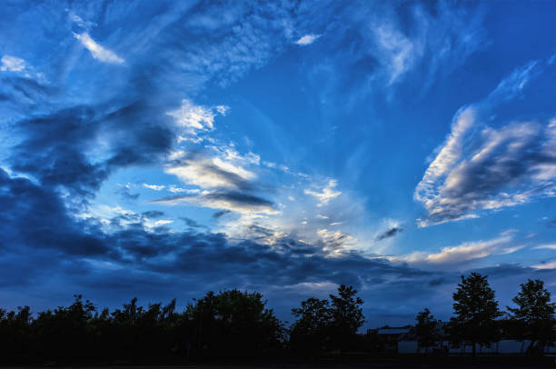 dark blue evening sunset sky with various clouds above the trees