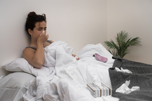 A sick woman, tissues in hand, holds medical drops in bed, fighting her illness.