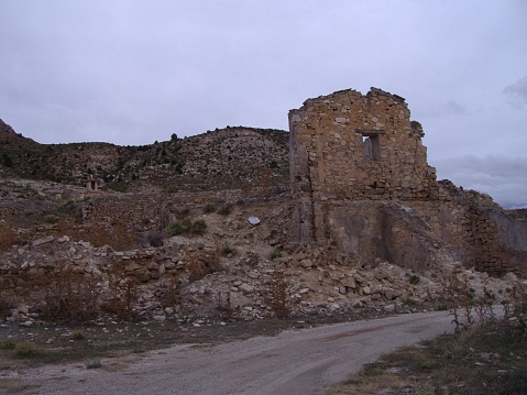 Stone house in ruins in an abandoned village, of which only one side of the façade remains. A view of a highway