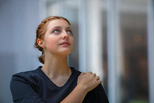 A hopeful young woman gazes skyward with confidence, her hand on her shoulder, embodying belief in the future. Portrait with space for inspiration.