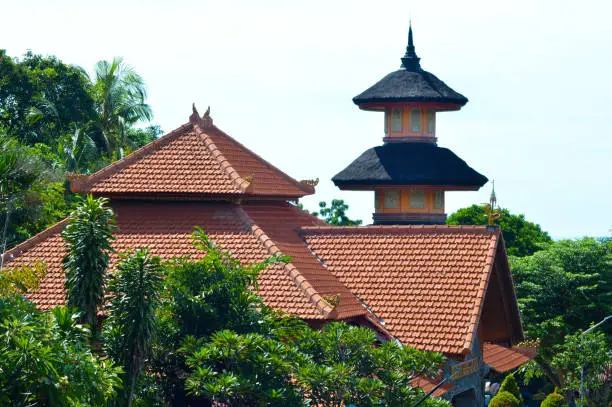View Of Tiled Roof Of Buddhist Temple Building And Multi-Tiered Top Of Pagoda Soaring Amidst The Trees Of The Garden