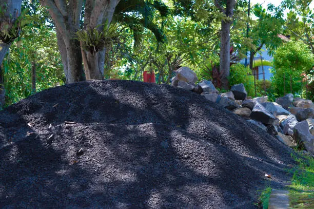 A Pile Of Sand And Stones Of Building Materials Amidst Trees And Plants In The Garden