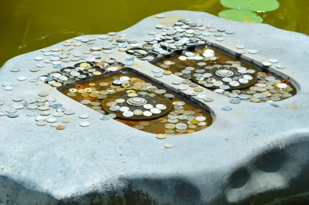 Close-Up High Angle View Of Artistic Regius Stone Relief Symbols Of Buddha's Footprint Adorned With Scattered Coins In The Garden Pond