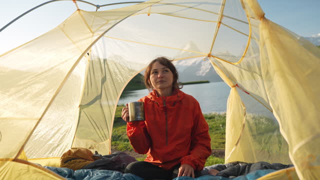 Woman drinking coffee in the tent near the idyllic lake in Swiss Alps