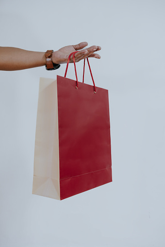 A male(man) hand hold a red shopping bag(paper bag) with red rope at the studio.